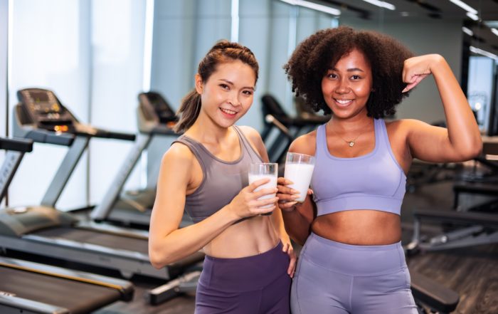 Two women dressed in sportswear after having trained in the gym, each with a glass of milk.