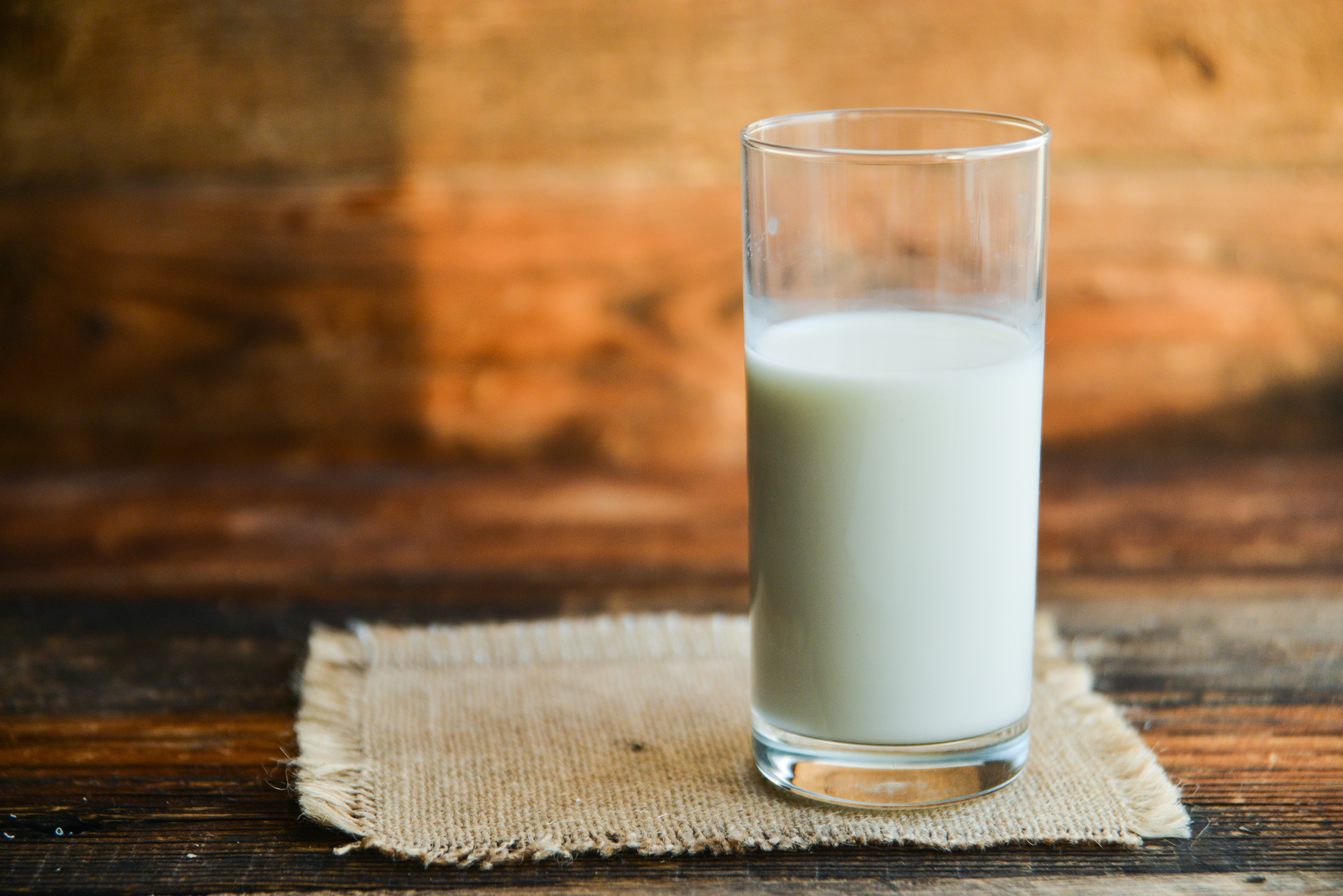 glass of white milk on burlap coaster with a wood background