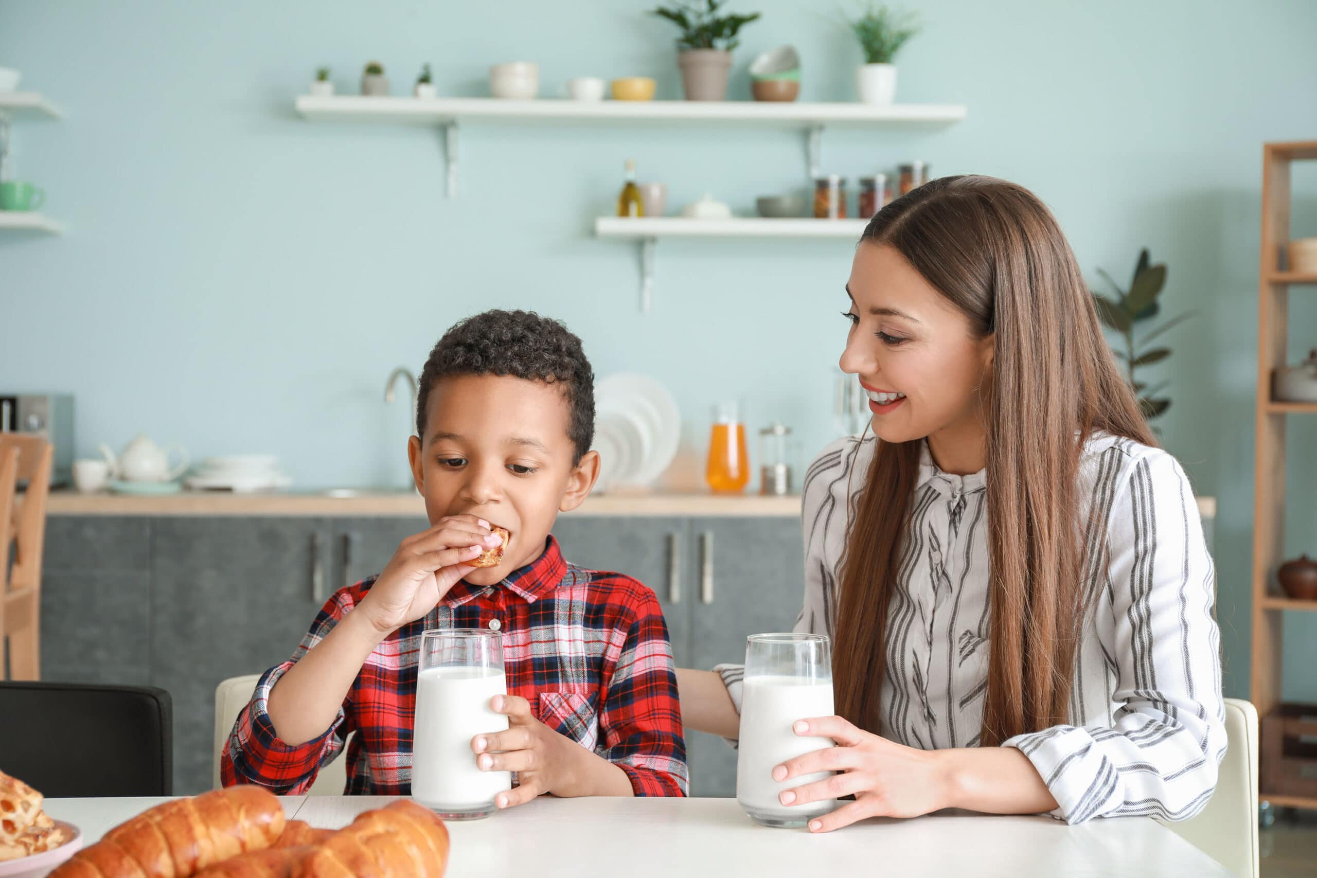 Woman watching a boy eat a cookie with milk