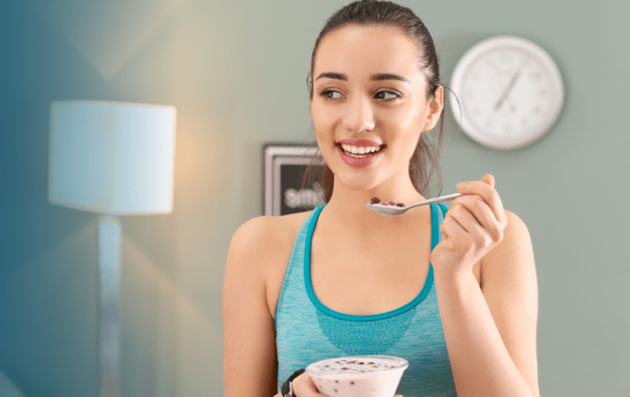 A woman holding a spoon and enjoying a yogurt with fruits after a home workout session.