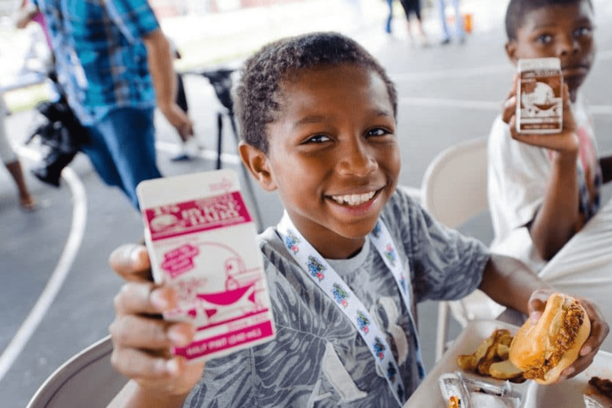 Two young children sitting in the schoolyard, enjoying a carton of milk as part of their school lunch.